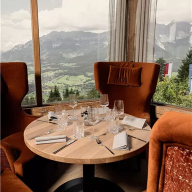 A stylish table in a restaurant with a view of the mountains. The cozy armchairs and the large window front create an inviting atmosphere.