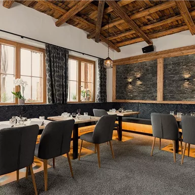 A modern restaurant with wooden beam ceilings and cozy seating areas. The elegant decor shows a beautiful contrast between stone walls and soft fabrics.