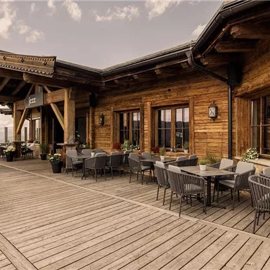 A cozy terrace with wooden cladding and modern chairs. In the background are large windows that offer a view of the surroundings.