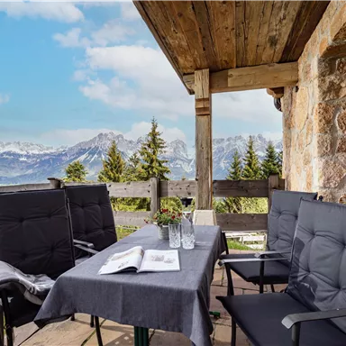 A cozy balcony with a table and chairs. In the background, impressive mountains and a clear sky can be seen.