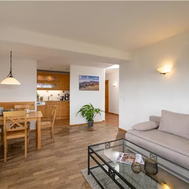 A bright living room with a cozy sofa and a dining table. The modern furniture and wooden floors create an inviting atmosphere.