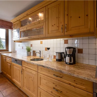 A cozy kitchen with wooden cabinets and a granite countertop. Glasses and a coffee machine are on the table.