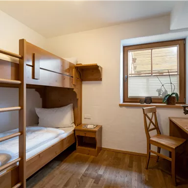 A simple room with bunk beds and a desk. Soft light falls on the wooden floor through the window.