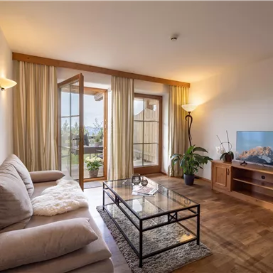 A cozy living room with a bright sofa and an elegant coffee table. Large windows bring in plenty of daylight and offer a beautiful view outdoors.