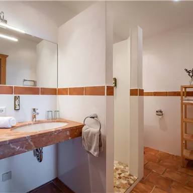 A modern bathroom with an elegant wooden sink and a glass shower. The walls are bright and the floor is tiled with warm tiles.