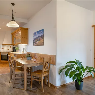 A bright kitchen with a dining table and chairs. In the background, we see an open living area and a plant.
