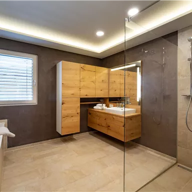 A modern bathroom with a shower and elegant wooden furniture. The walls are light and the lighting creates a pleasant atmosphere.