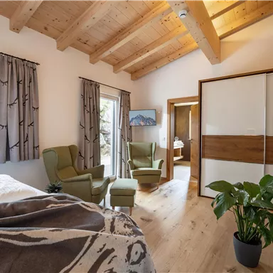A cozy room with a wooden ceiling and two comfortable armchairs. Large windows offer a view of nature, and a plant adds a fresh touch.