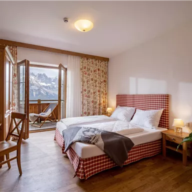 A cozy hotel room with a large double bed and a balcony. The room is modernly furnished and offers a view of the mountains.