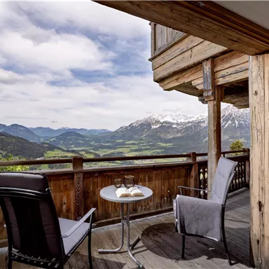 A cozy balcony overlooking the majestic mountains and green landscape. Two chairs and a table invite you to relax.