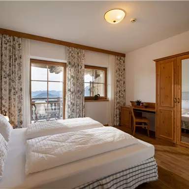 A cozy bedroom with two beds and wooden furnishings. Large windows offer a beautiful view of the surrounding landscape.