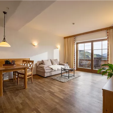 A cozy living room with a sofa, a dining table, and chairs. Large windows offer a view and natural light.