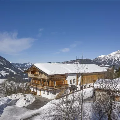 A picturesque chalet in a snowy winter landscape. In the background, snow-covered mountains stretch under a clear blue sky.