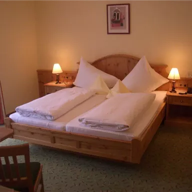 A cozy bedroom with a large double bed and two nightstands. The walls are painted in gentle colors, and there is a window with curtains.