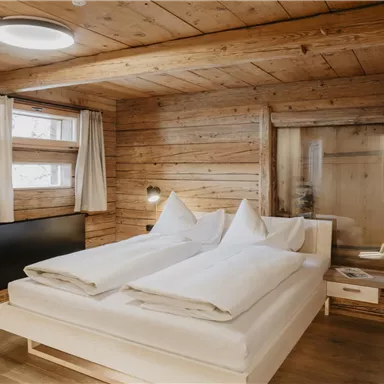 A cozy bedroom with wooden paneling. There is a large bed, white bedding, and windows with curtains.