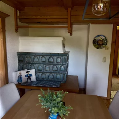 A cozy room with a wood stove and a dining table. On the table, there is a vase with flowers, and small decorative figures are visible.