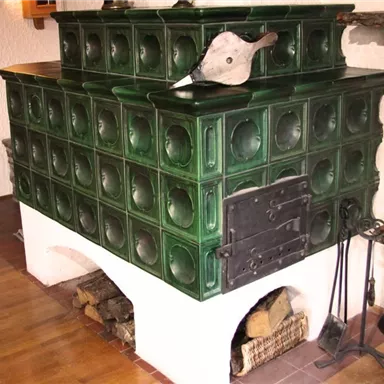 A traditional green tiled stove in a cozy room. The stove has a decorative surface and is heated with wood.