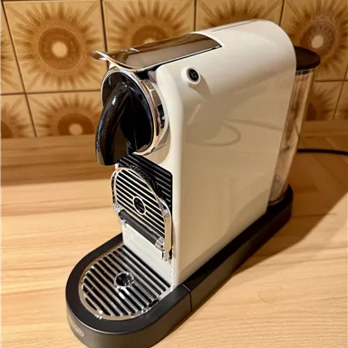 A stylish white coffee machine stands on a wooden sign. In the background, decorative tiles can be seen.