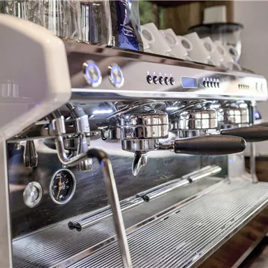 Eine moderne Espressomaschine mit glänzendem Edelstahl und mehreren Brühgruppen. Sie steht in einer gemütlichen Café-Umgebung.