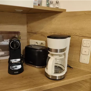 Eine moderne Küchenecke mit einer Kaffeemaschine, einem Toaster und einer Espressomaschine. Die Möbel sind aus hellem Holz und schaffen eine einladende Atmosphäre.