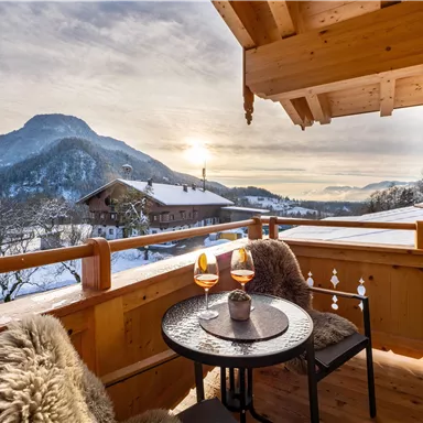 A cozy terrace with a view of the snow-covered mountains. On the table, there are two glasses as the sun sets.