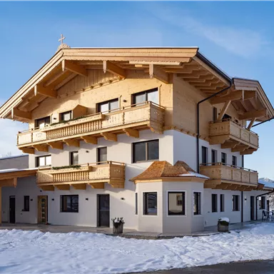 A modern building in alpine style with wooden cladding and several balconies. The surroundings are covered with snow and the sky is clear.