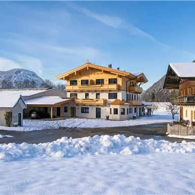 A charming alpine house in a snowy landscape. In the background, mountains and a clear blue sky can be seen.