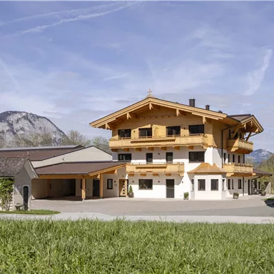 A picturesque building in alpine style, surrounded by green meadows and mountains. The sky is clear, and the landscape appears tranquil and inviting.
