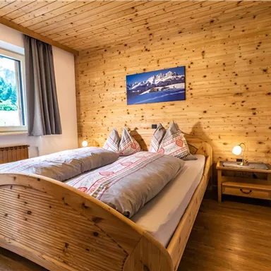 Ein gemütliches Schlafzimmer mit einem Holzbett und zwei Kissen. Die Wände sind aus Holz, und ein Fenster bietet einen Blick nach draußen.