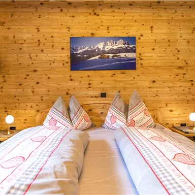 Ein gemütliches Schlafzimmer mit zwei Betten und Holzverkleidung. An der Wand hängt ein Bild von Berglandschaft und es gibt stilvolle Nachttischlampen.