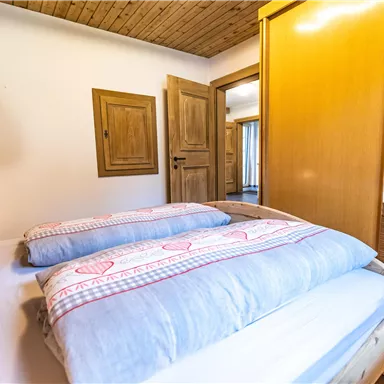 Ein gemütliches Schlafzimmer mit einem Bett, einer Holzdecke und einem Kleiderschrank. Die Wände sind in warmen Tönen gehalten, was eine einladende Atmosphäre schafft.