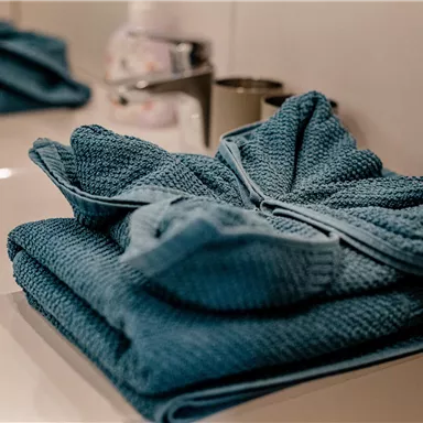 Ein modernes Badezimmer mit gestapelten blauen Handtüchern auf einem Waschbecken. Die Umgebung ist hell und sauber.