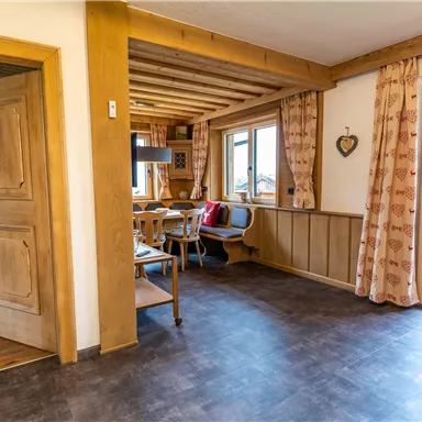 Ein gemütlicher Wohnraum mit Holzdetails und großen Fenstern. Es gibt einen Esstisch und Zugang zu einem Balkon.