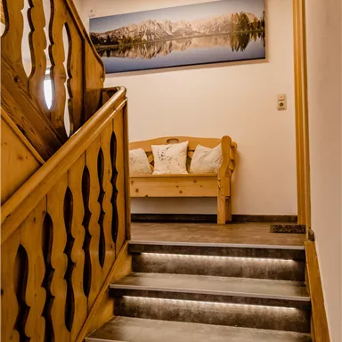 Ein gemütlicher Treppenbereich mit holzgefertigtem Geländer und einem modernen Bild an der Wand. Am Ende der Treppe befindet sich eine Holzbank mit Kissen.