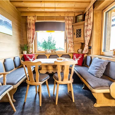 Ein gemütlicher Essbereich in einer Holz-Hütte. Der Raum ist mit bequemen Bänken und einem runden Tisch ausgestattet, ideal für gesellige Abende.