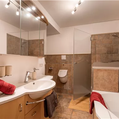 Ein modernes Badezimmer mit einer Dusche und einer Badewanne. Es gibt Holz- und Fliesenoberflächen sowie auffällige rote Handtücher.