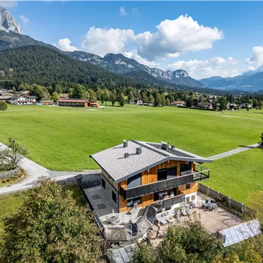 Ein modernes Haus in einer ländlichen Umgebung mit Blick auf die Berge. Das Grundstück ist umgeben von einer großen, grünen Wiese.