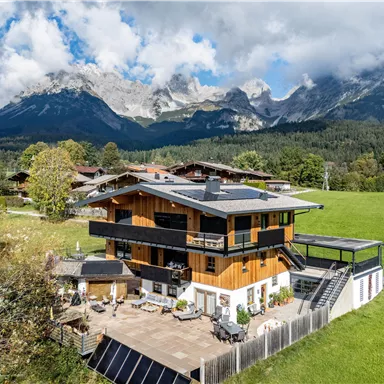 Ein modernes Haus in den Bergen mit einem großzügigen Außenbereich. Die Umgebung ist grün und die Berge sind majestätisch im Hintergrund sichtbar.