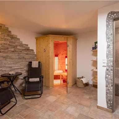 Ein gemütlicher Wellnessbereich mit einer Sauna, einem Dampfbad und stilvollen Liegestühlen. Die Wände sind mit Steinverkleidung dekoriert, und das Licht schafft eine entspannte Atmosphäre.