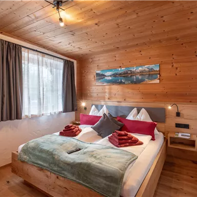 Ein gemütliches Schlafzimmer mit einem großen Bett und Holzwänden. Weiche Decken und Kissen in warmen Farben schaffen eine einladende Atmosphäre.