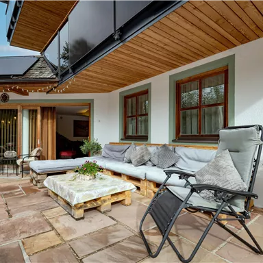 Eine gemütliche Terrasse mit Sitzgelegenheiten und einem modernen Holzüberstand. Die Umgebung ist hell und einladend, ideal zum Entspannen.