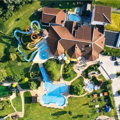 Ein großer Komplex mit mehreren Schwimmbecken und Rutschen umgeben von grünen Wiesen. Das Gebäude hat eine attraktive Architektur und lädt zum Entspannen ein.
