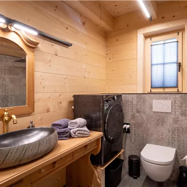 Ein modernes Badezimmer mit Holzwänden und eleganten Armaturen. Es enthält ein Waschbecken, Toiletten und eine Dusche.