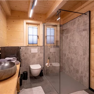 Ein modernes Badezimmer mit Holzvertäfelung und einer großen Dusche aus Glas. Der Waschbecken ist stilvoll und rund, und es gibt Fenster, die für natürliches Licht sorgen.