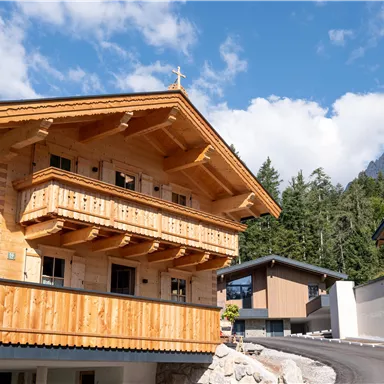 Ein traditionelles Holzhaus in den Bergen mit einem schönen Balkon und Kufstein-Landschaft im Hintergrund. Die klare Himmel und die umliegenden Bäume verleihen der Szene eine idyllische Atmosphäre.