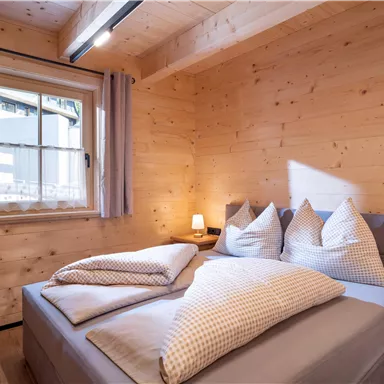 Ein gemütliches Schlafzimmer mit Holzvertäfelung und einem großen Bett. Es gibt Kissen und eine kleine Nachttischlampe neben dem Bett.