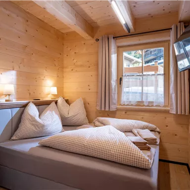 Ein gemütliches Schlafzimmer mit Holzvertäfelung, einem Doppelbett und großen Kissen. Das Zimmer hat ein Fenster mit Blick nach draußen und einen Fernseher an der Wand.
