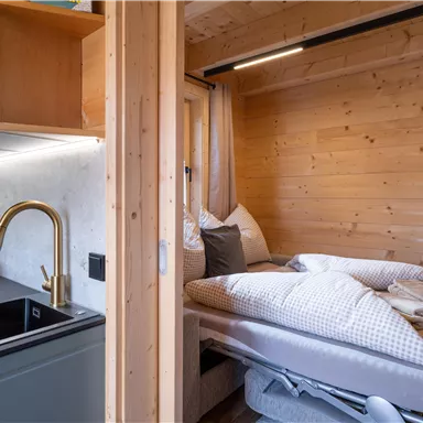 Eine gemütliche Holzzimmer mit einem Bett und einer modernen Küchenzeile. Das Licht ist warm und schafft eine einladende Atmosphäre.