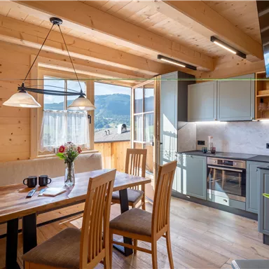 Eine gemütliche Küche mit Holzdecken und einem großen Esstisch. Die Fenster bieten einen schönen Blick auf die Landschaft.