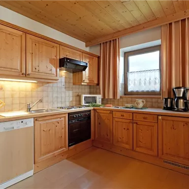 Eine gemütliche Küche mit Holzschränken und modernen Geräten. Die Fenster lassen viel natürliches Licht herein.